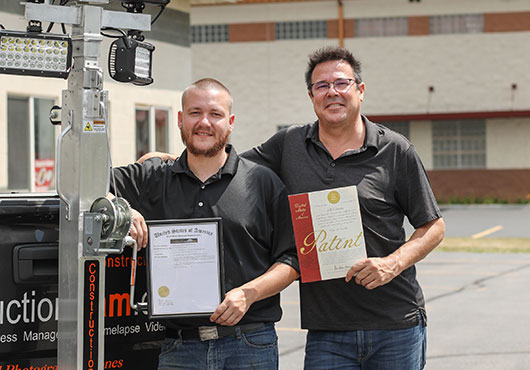 Father and son, Mark Carroll (right) and Kyle Carroll, show off the patent and trademark certificates for their REESE hitch light tower system.